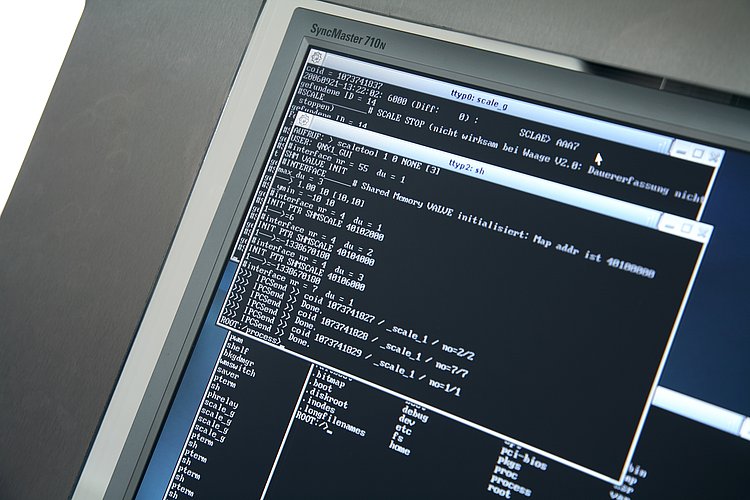 Various console windows are visible on the monitor, displaying system logs and commands in a programming environment.