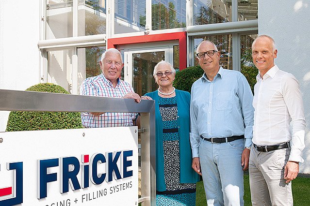 The owner family stands smiling in front of the Fricke company building, surrounded by well-kept greenery and modern design.