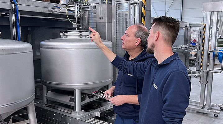 In der Produktion von FRICKE zeigen zwei Männer auf eine Dosieranlage, während sie sich über die Funktionsweise austauschen.