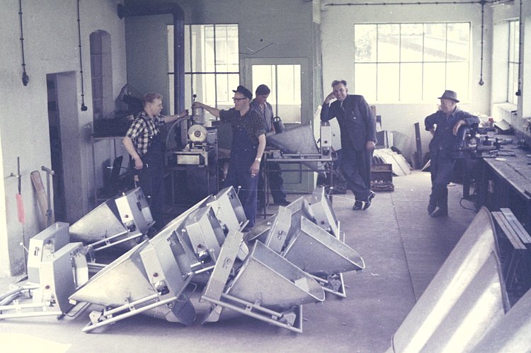 The scene shows men in work clothes surrounded by various machines.