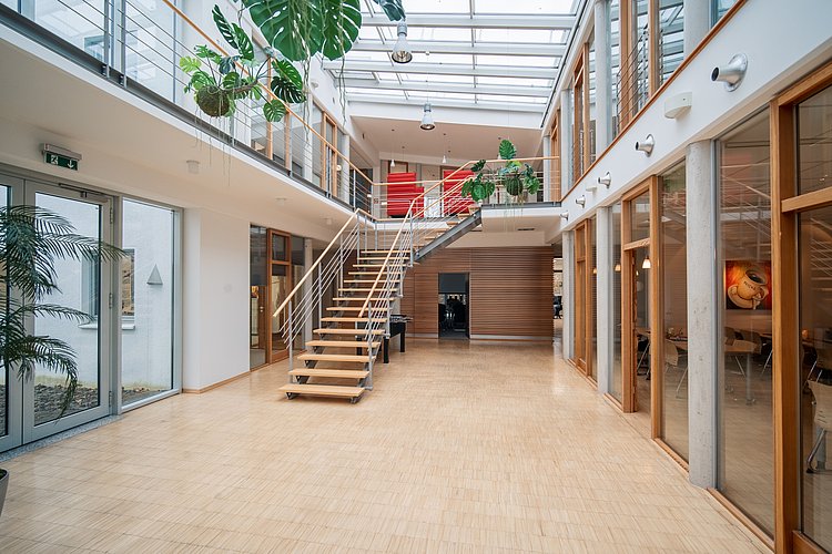 The interior of FRICKE is flooded with light, featuring an elegant staircase and plants that create a fresh, modern environment.