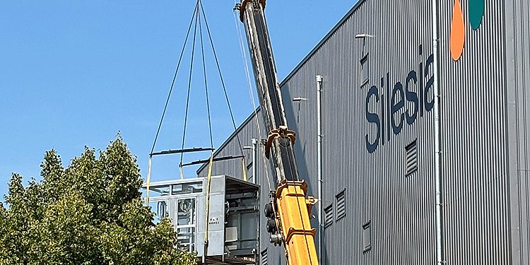 Ein Kran hebt eine große FRICKE Anlage, während sie über das Gebäude mit der Aufschrift 'Silesia' schwebt.