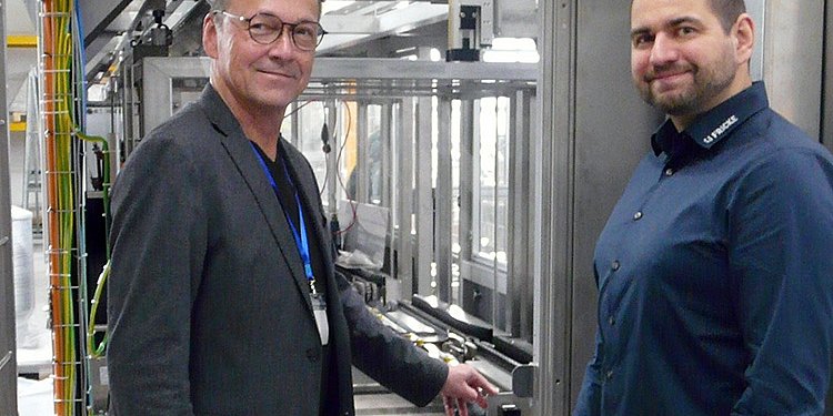 Die Männer lächeln in einer hochmodernen Produktionsstätte, während sie an einer Dosieranlage stehen, die für die Parfüm- und Aromenproduktion konstruiert ist. dacht ist.