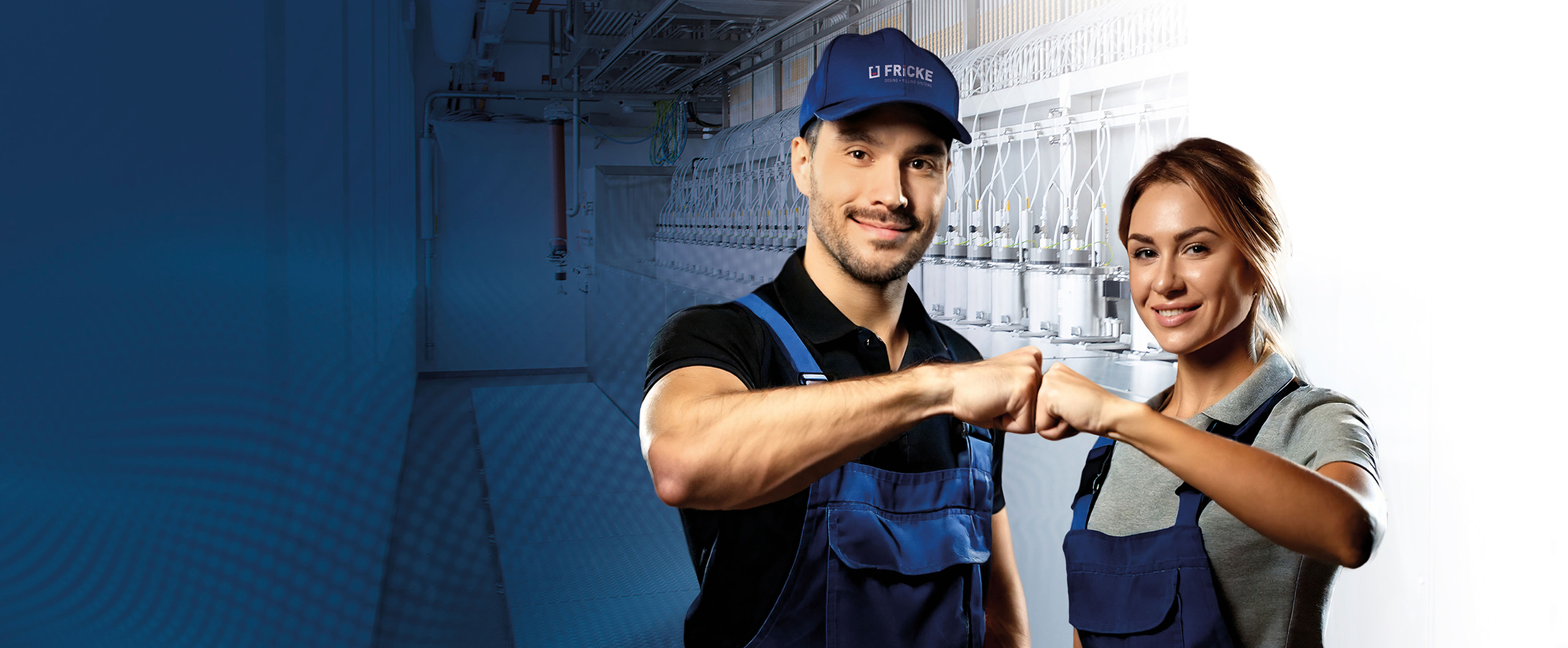 Zwei junge Handwerker, ein Mann und eine Frau, geben sich lächelnd ein fist bump vor einem Produktionshintergrund.