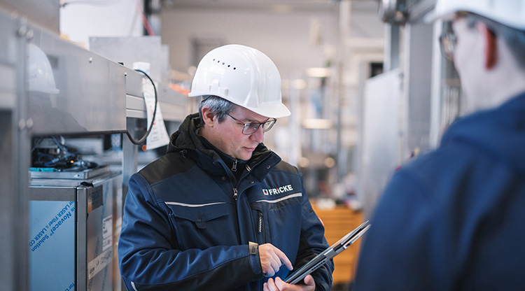 The employee analyzes data on a tablet while standing in an industrial environment.