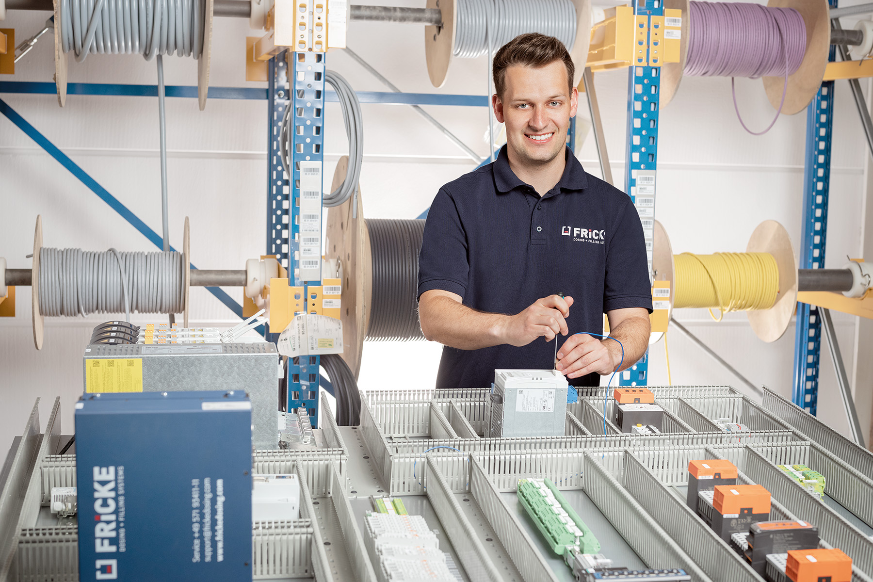 A friendly electrician stands at a table full of electrical components and cables while he carries out an installation.