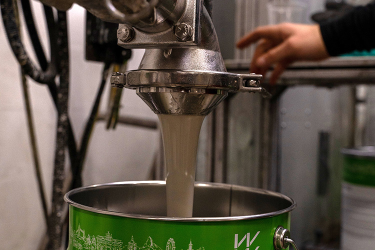 Flüssigkeit strömt aus einem Abfüllventil in einen grünen Eimer, während eine Hand in der Nähe den Prozess unterstützt.