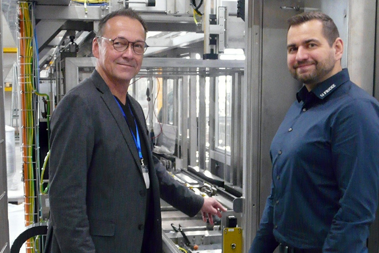 Die Männer lächeln in einer hochmodernen Produktionsstätte, während sie an einer Dosieranlage stehen, die für die Parfüm- und Aromenproduktion konstruiert ist. dacht ist.