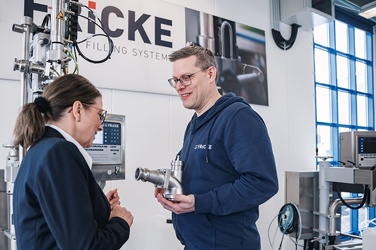 Die Interaktion zwischen dem Mann und der Frau deutet auf eine technische Beratung hin, umgeben von modernen Maschinen und Geräten.