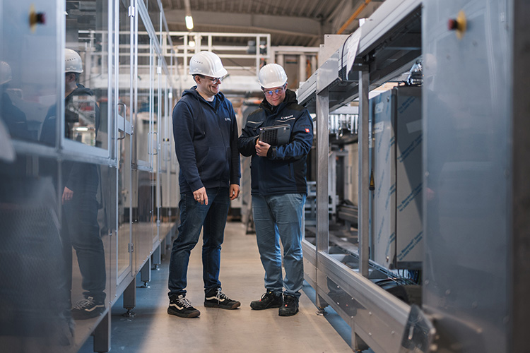 Ein freundliches Gespräch zwischen zwei Technikern in einer Fabrik, während sie sich auf ein Tablet konzentrieren.