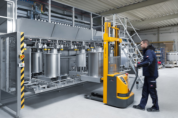 Ein Arbeiter steuert einen Gabelstapler in einer modernen Produktionshalle mit großen, silbernen Behältern.