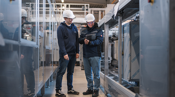 A friendly conversation between two technicians in a factory as they focus on a digital device.
